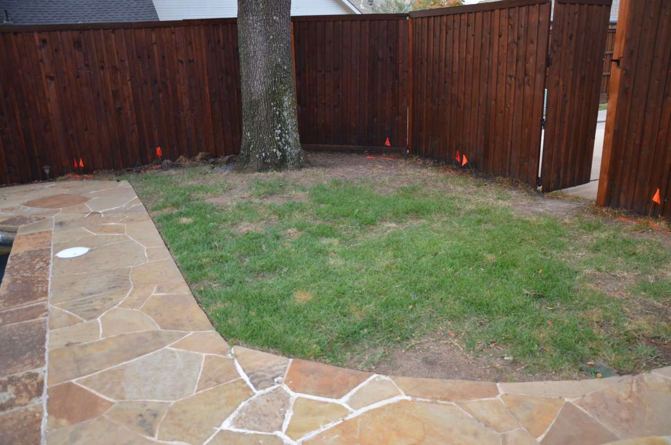 Before: a fenced corner of a yard beside a flagstone patio