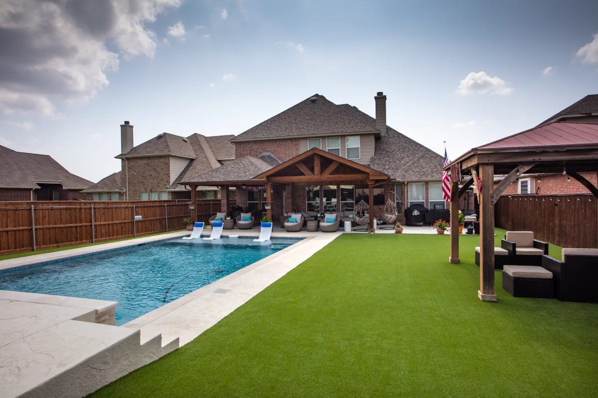 A finished backyard with turf laid up to the pool deck and pavilion